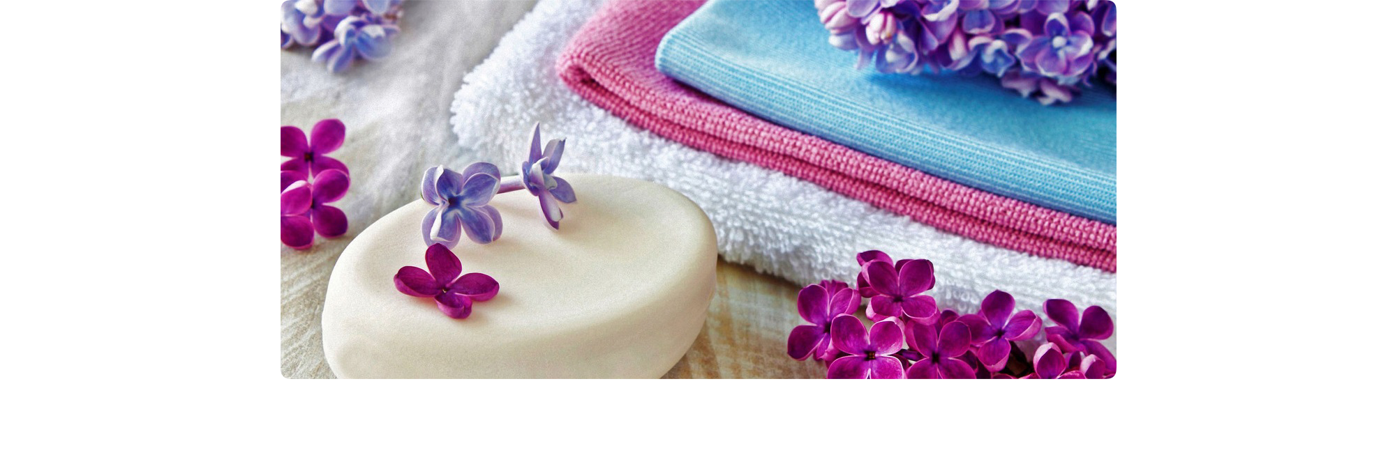 Set of clean white towels with a bar of soap in front and flower petals on top